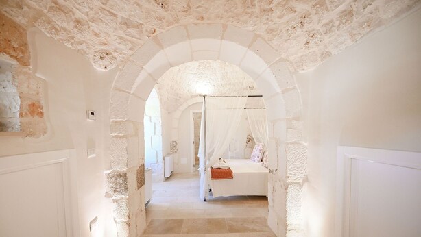 A narrow hallway with an arched ceiling leading to a bedroom with a bed and a canopy. - My Rental Homes - Trulli Heaven with private pool and large garden (San Michele Salentino)