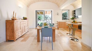 A modern kitchen with a wooden cabinet, a dining table set for four, and a view of the outdoors. - My Rental Homes - Trulli Heaven with private pool and large garden (San Michele Salentino)