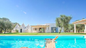 A poolside area with a clear view of a modern house, a grassy lawn, and a tree. - My Rental Homes - Trulli Heaven with private pool and large garden (San Michele Salentino)
