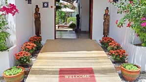 A hotel entrance with a 'WELCOME' mat, two wooden statues, and potted plants on either side. - vivi bungalows resort5 (Rawai)