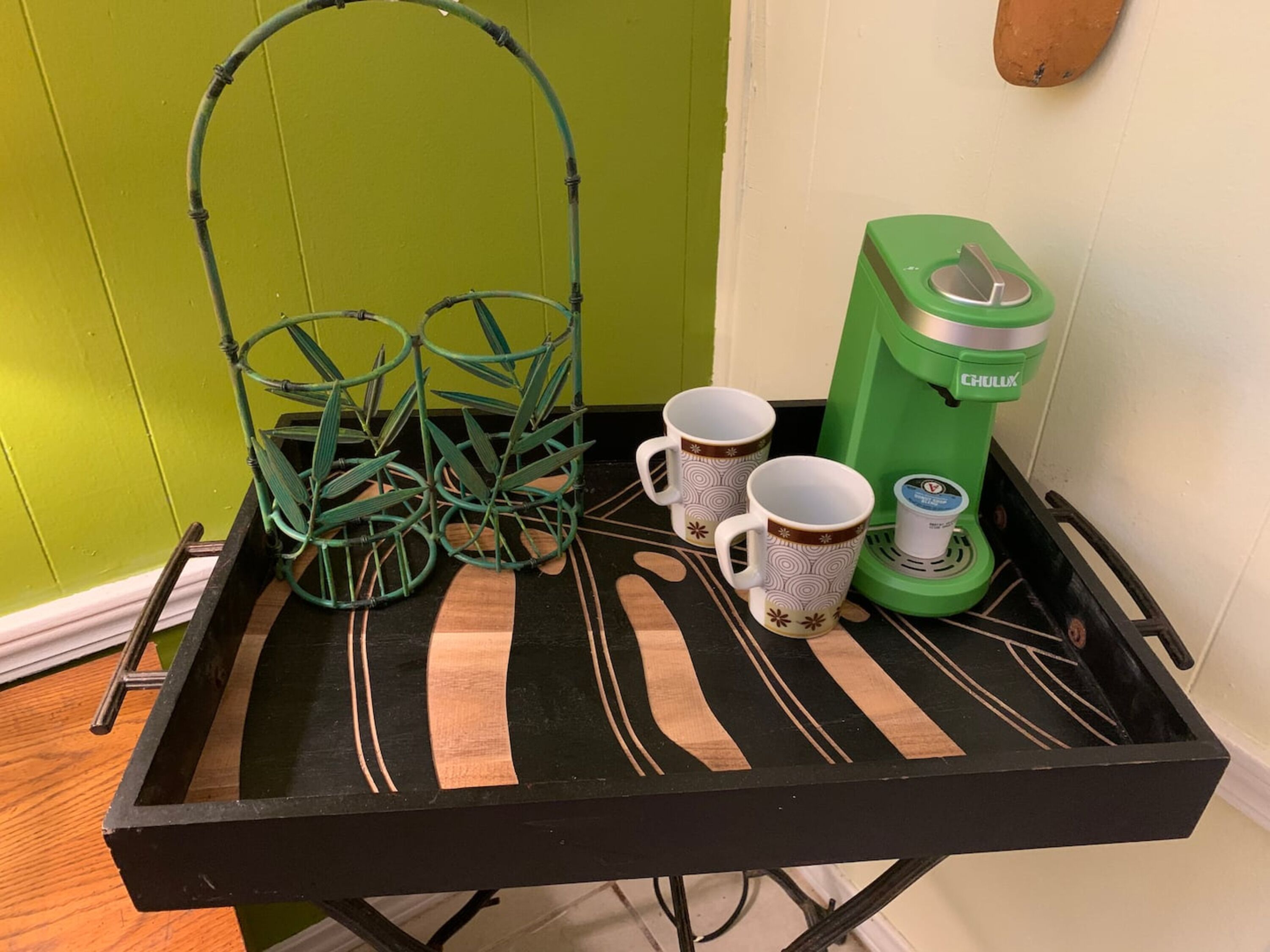 Un plateau avec deux tasses à café et une cafetière verte, le tout posé sur un support en métal noir.