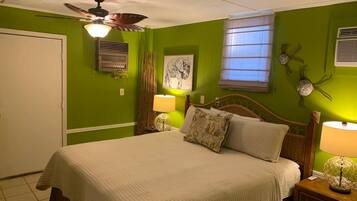 A bedroom with a bed, a ceiling fan, a window with blinds, and a wall-mounted air conditioning unit.