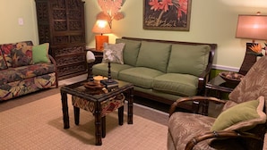 Ein Wohnzimmer mit einem grünen Sofa, einem gemusterten Sessel, einem Holztisch und einer dekorativen Lampe.