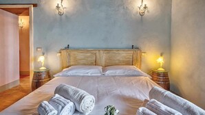 Ein Schlafzimmer mit einem Holzkopfteil, zwei Nachttischlampen und gerollten Handtüchern auf dem Bett.