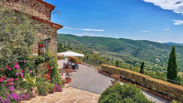 Ein Steingebäude mit Terrasse, Außenbestuhlung und Blick auf eine hügelige Landschaft.