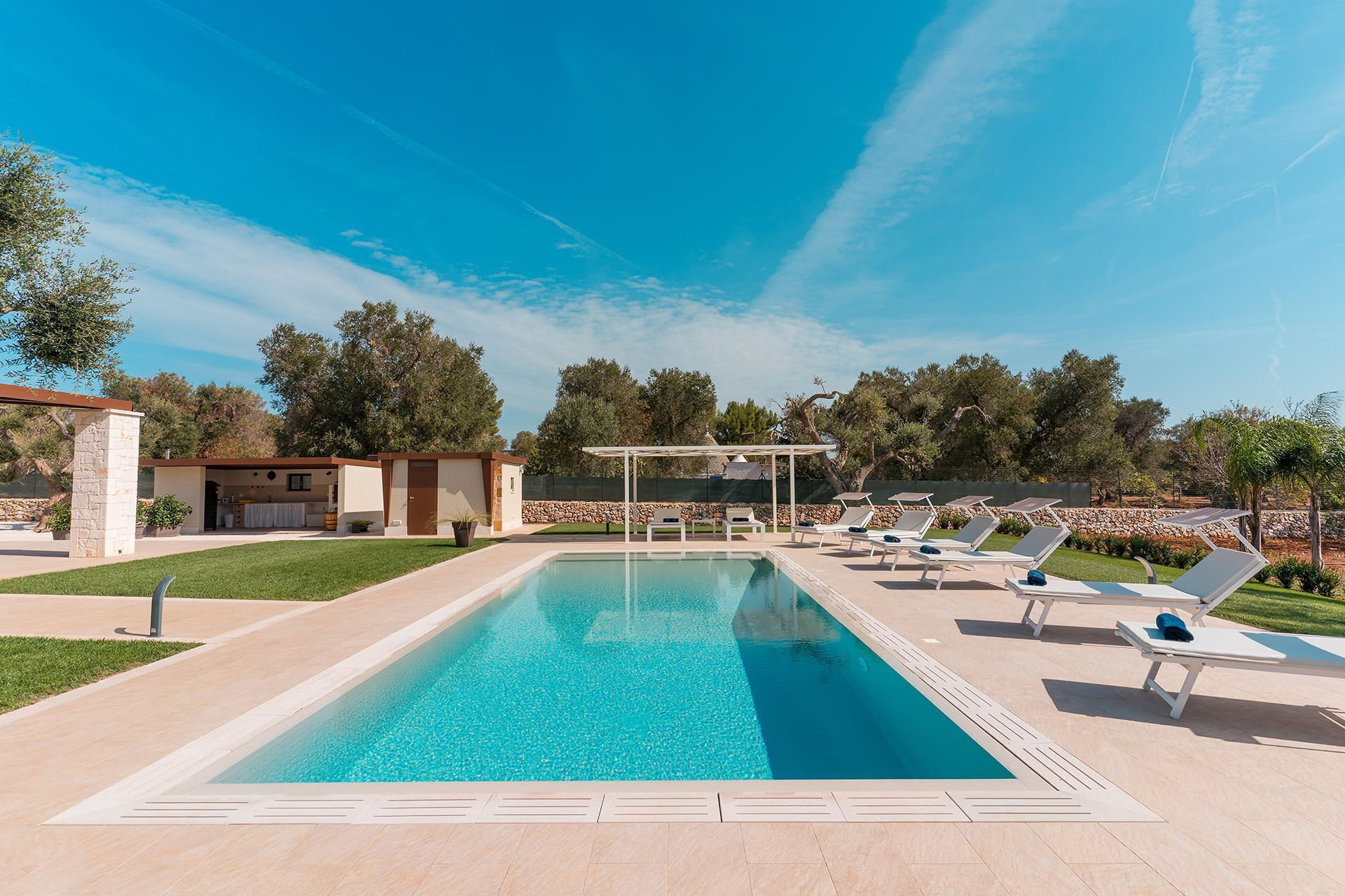 Una piscina rettangolare con una pergola e poltrone relax.