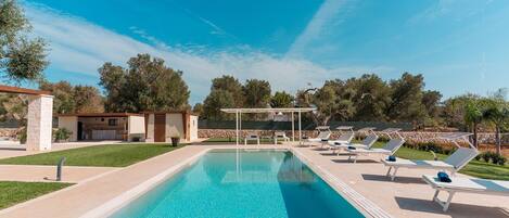 Una piscina rettangolare con una pergola e poltrone relax.