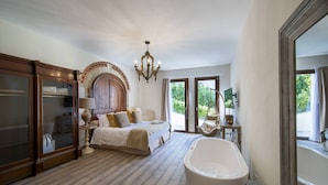 A spacious bedroom with a large bed, a hanging chair, a bathtub, and a view of greenery outside. - Villa Serena with private pool - My Rental Homes (Greve In Chianti)