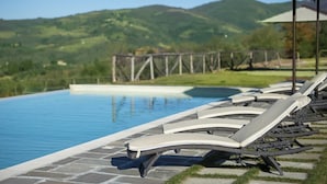 A poolside area with lounge chairs and a view of a mountainous landscape. - Villa Serena with private pool - My Rental Homes (Greve In Chianti)