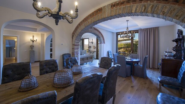 A dining area with a wooden table, upholstered chairs, and a chandelier. - Villa Serena with private pool - My Rental Homes (Greve In Chianti)