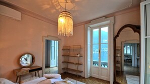 Een slaapkamer met een bed, een kroonluchter, een grote spiegel en uitzicht op zee door een deur.
