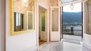 Een hal met een grote, versierde spiegel, een groene deur en uitzicht op een meer met bergen.
