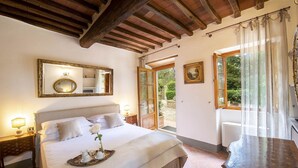 A bedroom with a large bed, a wooden ceiling, a window with curtains, and a painting on the wall. - Villa Grevigiana pool and SPA - My Rental Homes (Greve In Chianti)