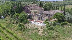 A stone villa with a terrace and outdoor seating area surrounded by greenery and hills. - Villa Grevigiana pool and SPA - My Rental Homes (Greve In Chianti)