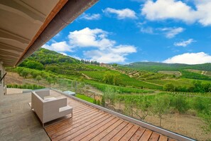 Un balcon doté d’un canapé en osier et d’une balustrade en verre, offrant une vue sur un vignoble.