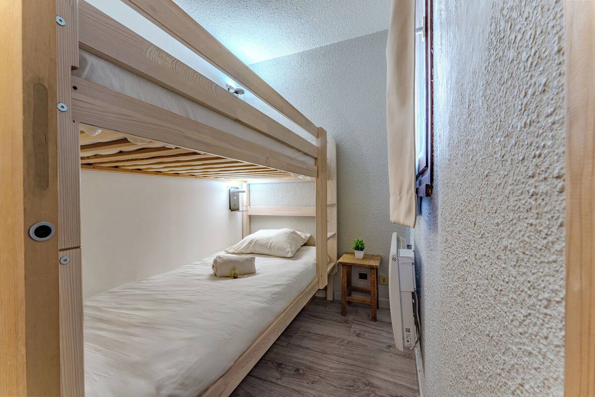A bunk bed room with a wooden headboard, a small bedside table with a plant, and a wall-mounted light.