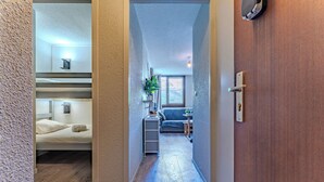 Un couloir étroit mène à une chambre dotée de lits superposés, d’une petite kitchenette et d’un espace de vie comprenant un canapé et une fenêtre.