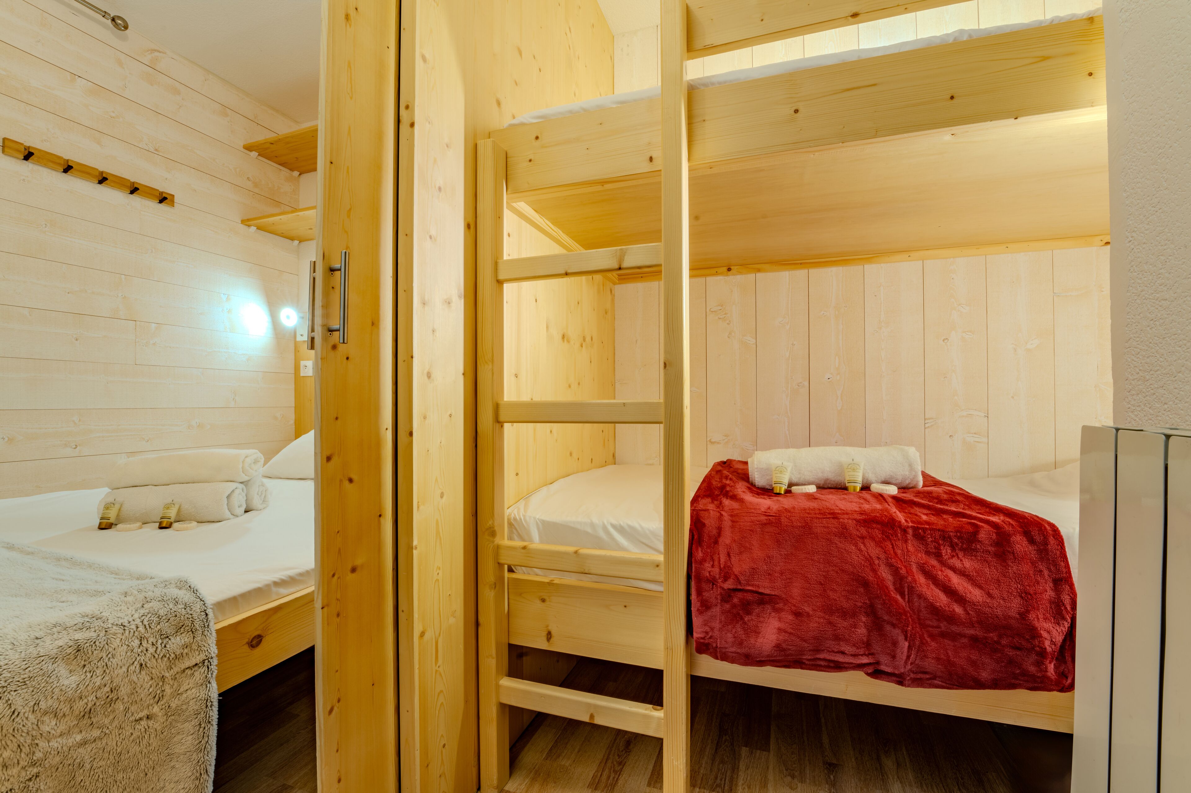 A wooden room with bunk beds, a small table, and a wall-mounted shelf.
