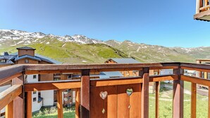 Un balcon en bois, orné de motifs en forme de cœur, qui offre une vue sur un paysage montagneux aux sommets enneigés.
