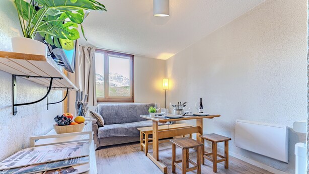 Un espace de vie compact comprenant un coin repas, un canapé, une table avec des chaises, un radiateur et une fenêtre donnant sur les montagnes.