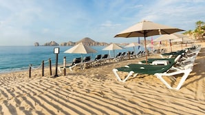 Una playa con filas de tumbonas y sombrillas, una vista despejada del mar y formaciones rocosas al fondo.