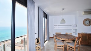 Ein Balkon mit Blick auf das Meer, ein runder Holztisch mit Stühlen, eine Hängeleuchte und eine weiße Regaleinrichtung.
