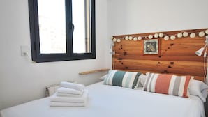 Ein ordentlich bezogenes Bett mit weißen Laken, ein Holzkopfteil mit Verzierungen und ein Fenster mit Jalousien.