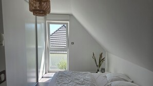 Una camera da letto con un letto, un comodino, una lampada e una finestra vista su un edificio.