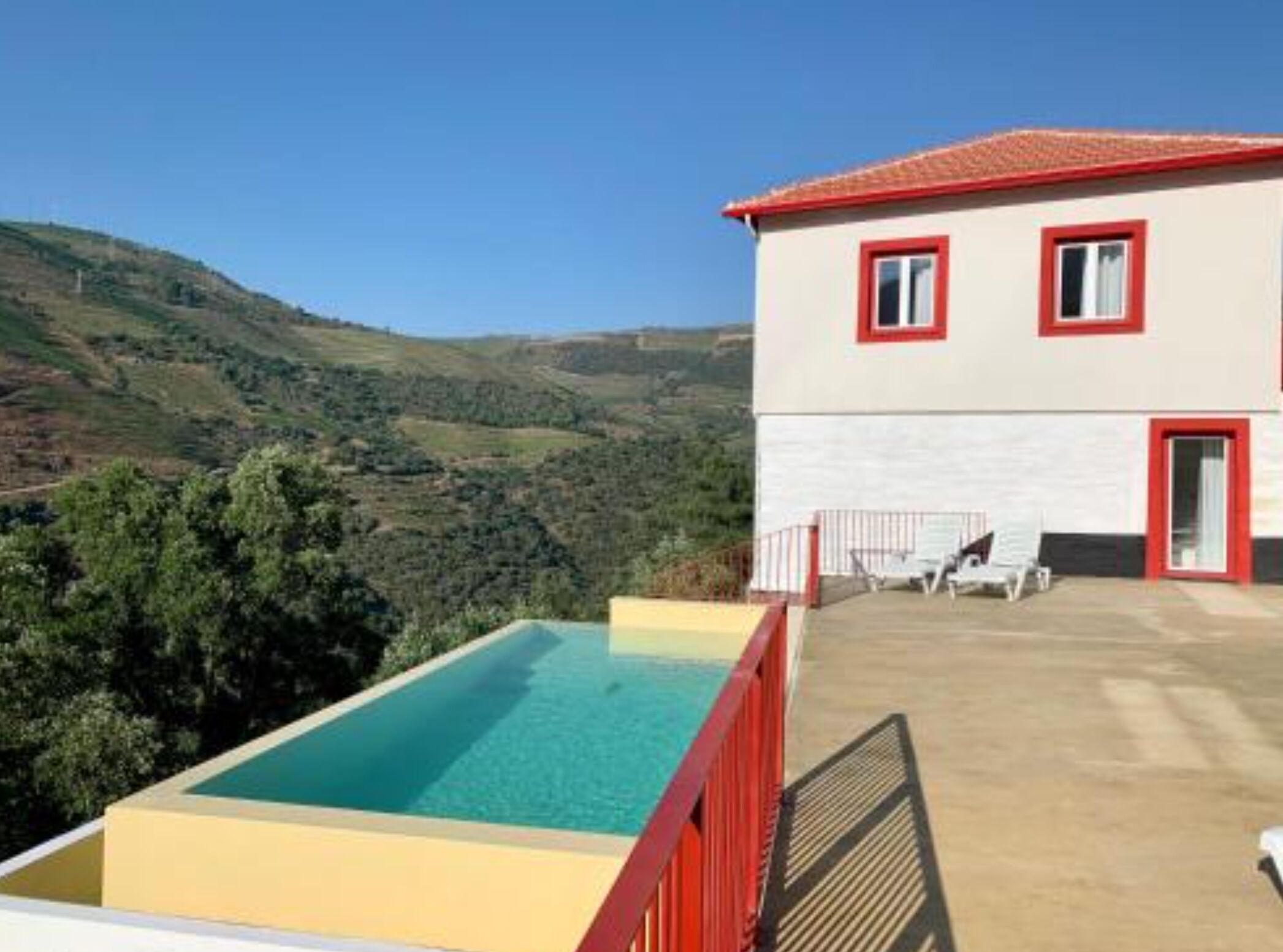 A two-story building with a red and white exterior, a swimming pool, and a view of hilly terrain.