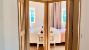 A narrow hallway leading to a bedroom with a bed, a small table, and a window with curtains. - Terraços do Távora - 2 Bedroom Apartment (Barcos)