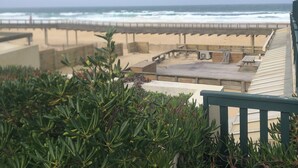 Een terras aan het strand met uitzicht op de oceaan, met een houten terras en zitgedeeltes.