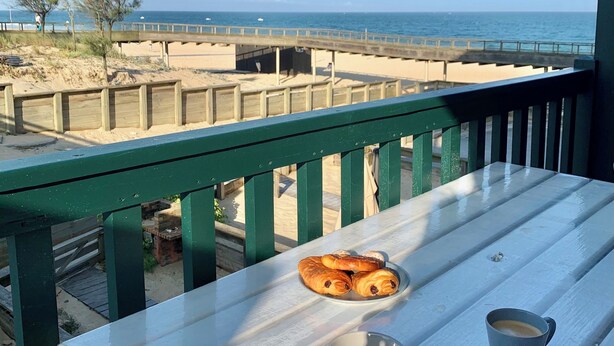 Een tafel met gebak en een kop koffie, met uitzicht op een strand en de oceaan.