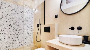 Ein modernes Badezimmer mit einem weißen Waschbecken, einer Toilette und einer Duschkabine mit gesprenkelten Fliesen.