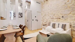 Ein modernes Zimmer mit einer Steinwand, einem weißen Sofa mit gestreiften Kissen, einem Holzessttisch, der für sechs Personen gedeckt ist, und einem grünen Sessel.