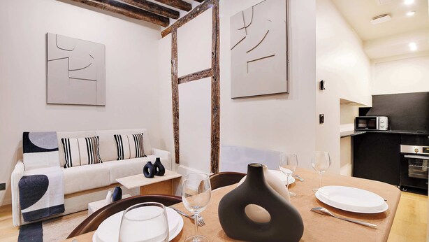 Un comedor moderno con una mesa de madera dispuesta para dos personas, un sofá con cojines a rayas y arte abstracto en la pared.