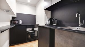 Una cocina moderna con armarios negros, horno empotrado, microondas y cafetera.