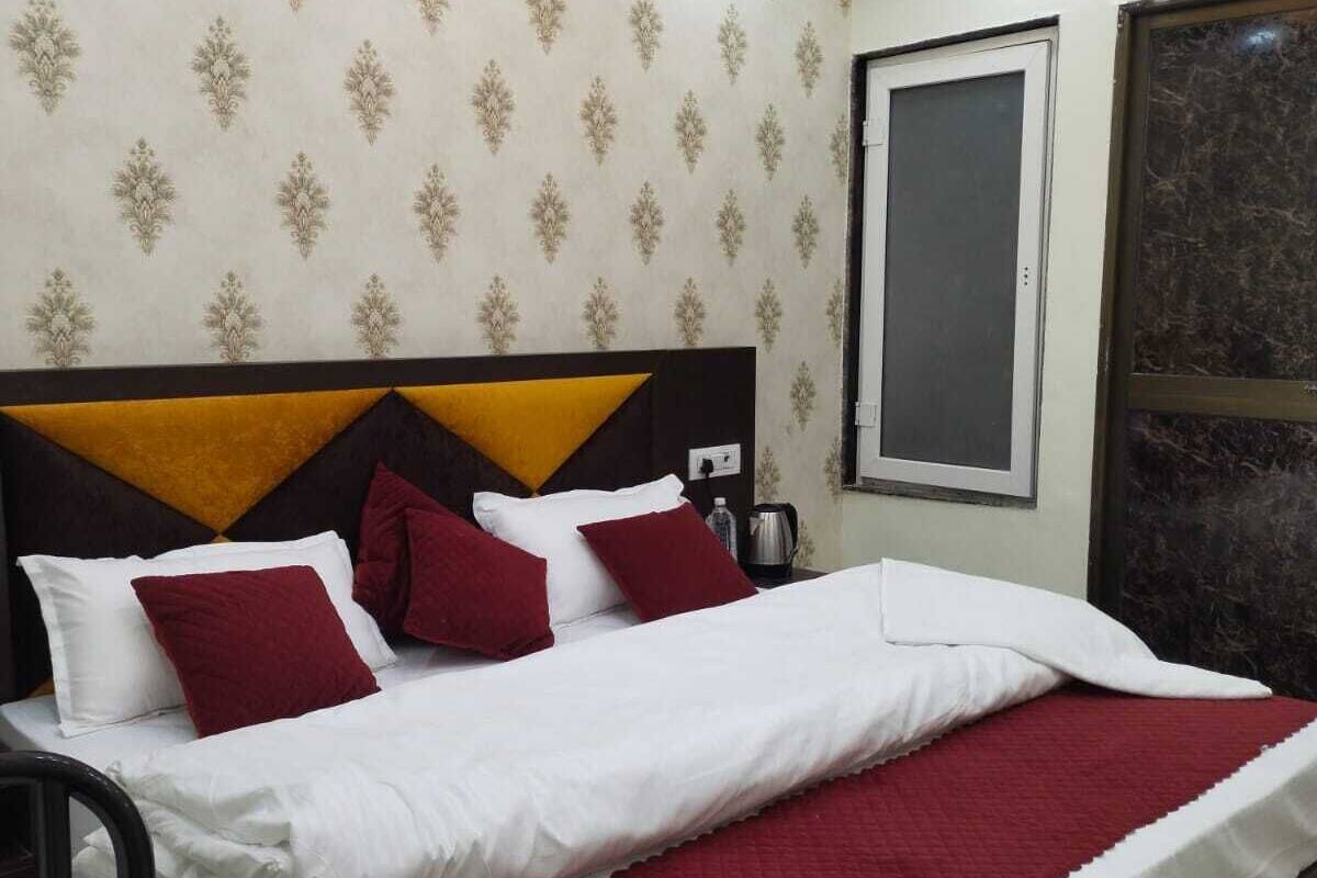 A neatly made bed with white and red bedding, a headboard with a geometric design, and a patterned wallpaper.