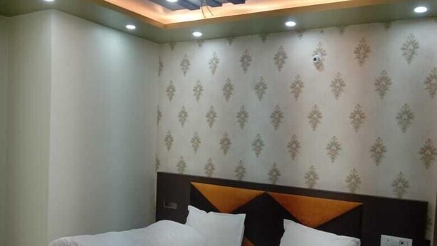 Ein ordentlich bezogenes Bett in einem Hotelzimmer mit gemustertem Wandpapier, einer modernen Deckenleuchte und einem Nachttisch mit Lampe.