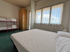 A room with a bunk bed, a wardrobe, a single bed, and a window with curtains. - 2 Sea View Penthouse with Large Balcony (Bellaria-Igea Marina)