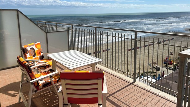 A balcony with a table and chairs, overlooking a beach with waves and a clear sky. - 2 Sea View Penthouse with Large Balcony (Bellaria-Igea Marina)