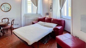 A bedroom with a bed, a red leather sofa, a small table with chairs, a mirror, and two windows with curtains. - Inn Pantheon home lovely apartment 50 meters from the Pantheon (Roma)