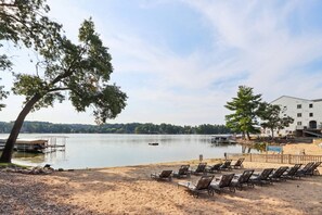 A lakeside view with a row of beach chairs, a dock, and a building in the background.