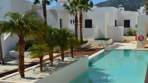 Una piscina con cubierta de madera, rodeada de muros blancos y palmeras.
