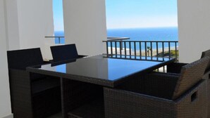 Un balcón con vista al océano, una mesa de vidrio y mobiliario de mimbre.