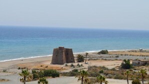 Vista costera con una estructura de piedra cerca de la playa, palmeras y cielo despejado.