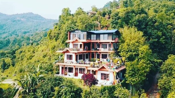 A multi-story building with balconies, surrounded by lush greenery and hills.