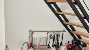 A kitchen with a sink, wooden countertop, and hanging utensils. There is a staircase with wooden steps and black metal railings.
