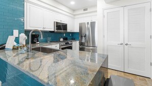 Eine moderne Küche mit weißen Schränken, einer Granit-Arbeitsplatte, Edelstahlgeräten und einer blauen Spritzschutzwand.