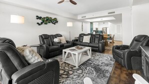 Ein geräumiges Wohnzimmer mit schwarzen Ledersofas, einem weißen Couchtisch und einem Deckenventilator.