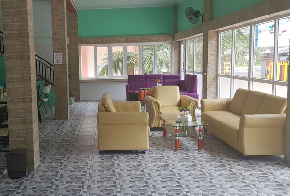 A spacious lobby with a checkered floor, large windows, and a seating area with yellow sofas and a purple couch. - Hotel Mega Nasional (Nias)